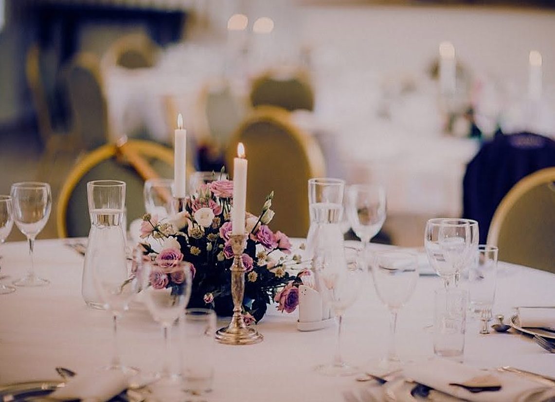 Mesa de gala con copas, velas y arreglo floral en un evento
