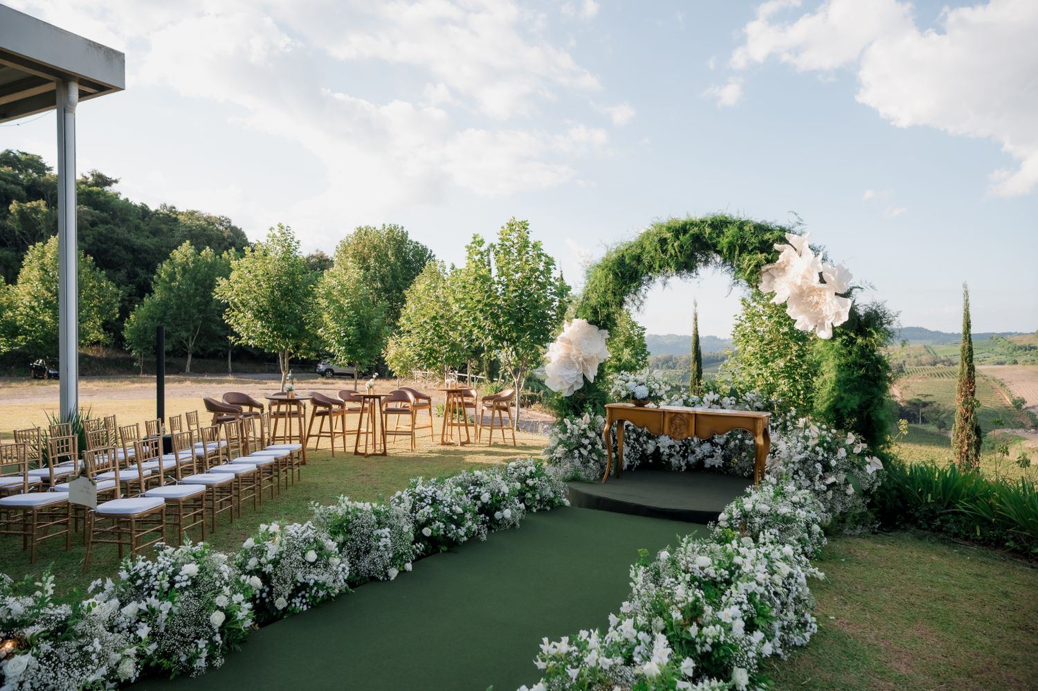 Montaje de ceremonia al aire libre con arco floral y sillas blancas en un jardín
