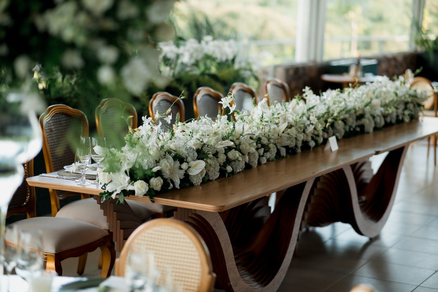 Mesa larga decorada con follaje verde y flores blancas para un banquete